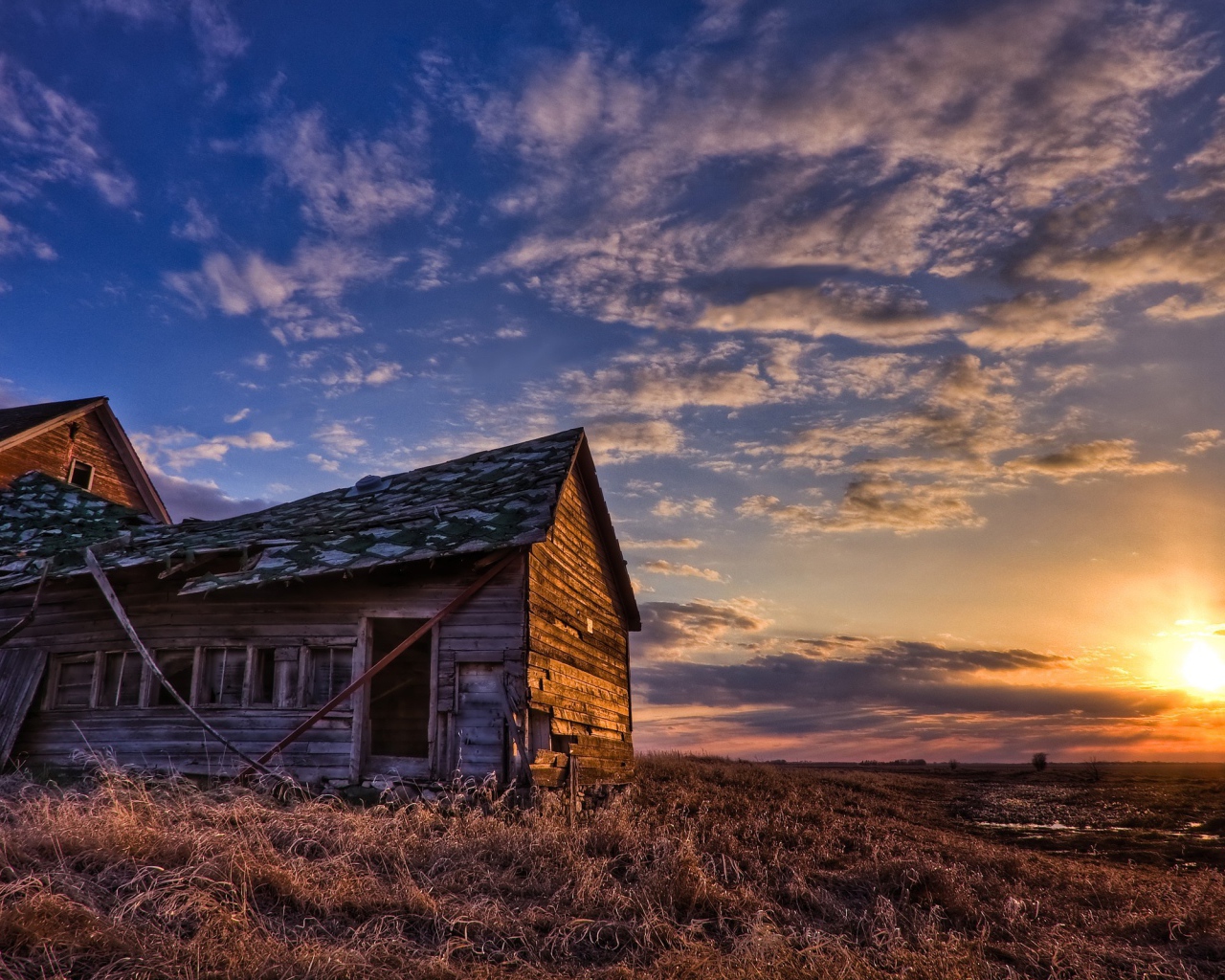 Деревянный домик с разрушенной крышей на фоне заката