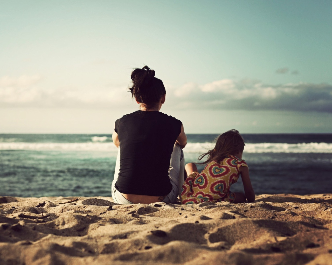 A woman and her daughter sitting in the sand on the beach