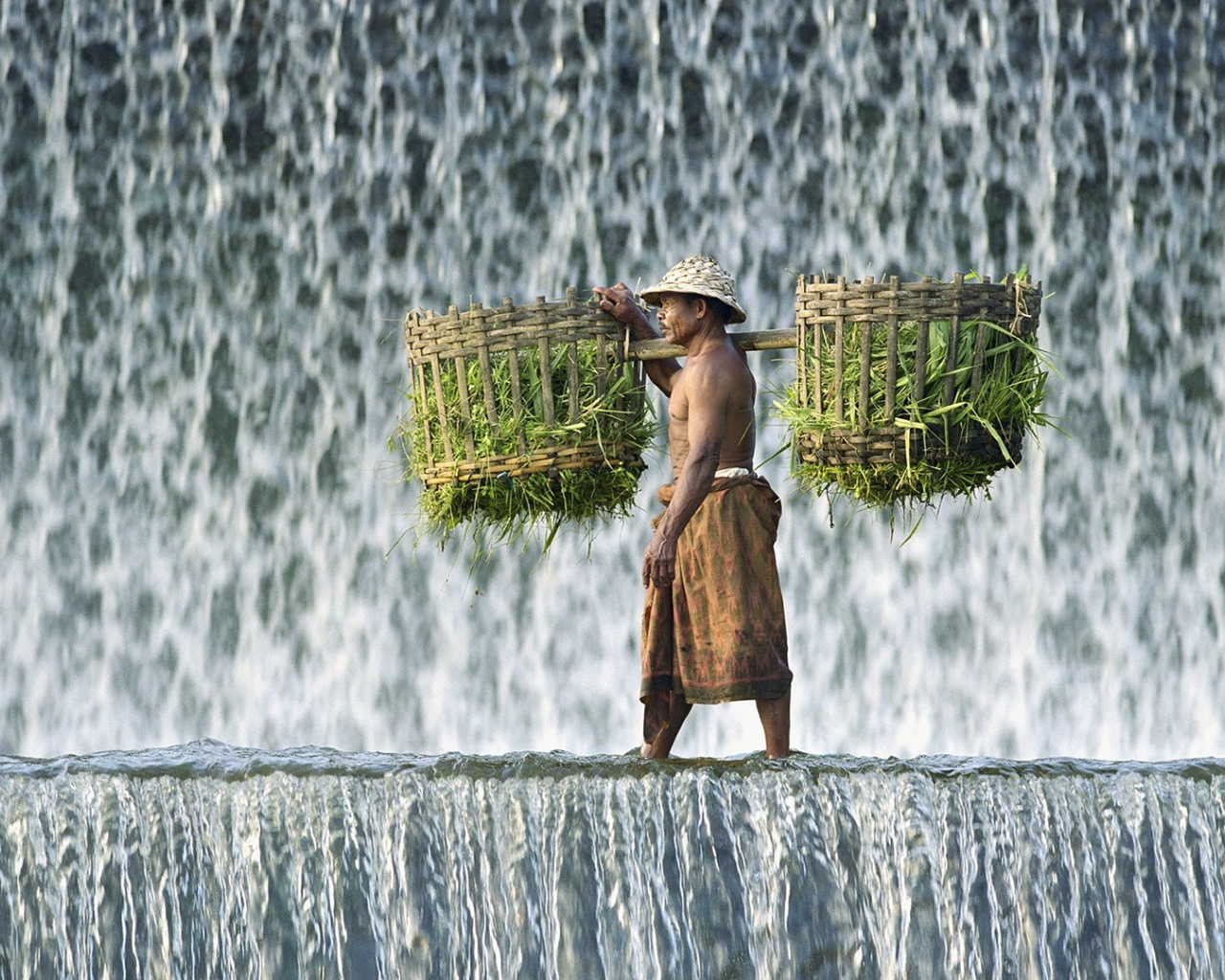 Крестьянин с корзинами идет по водопаду