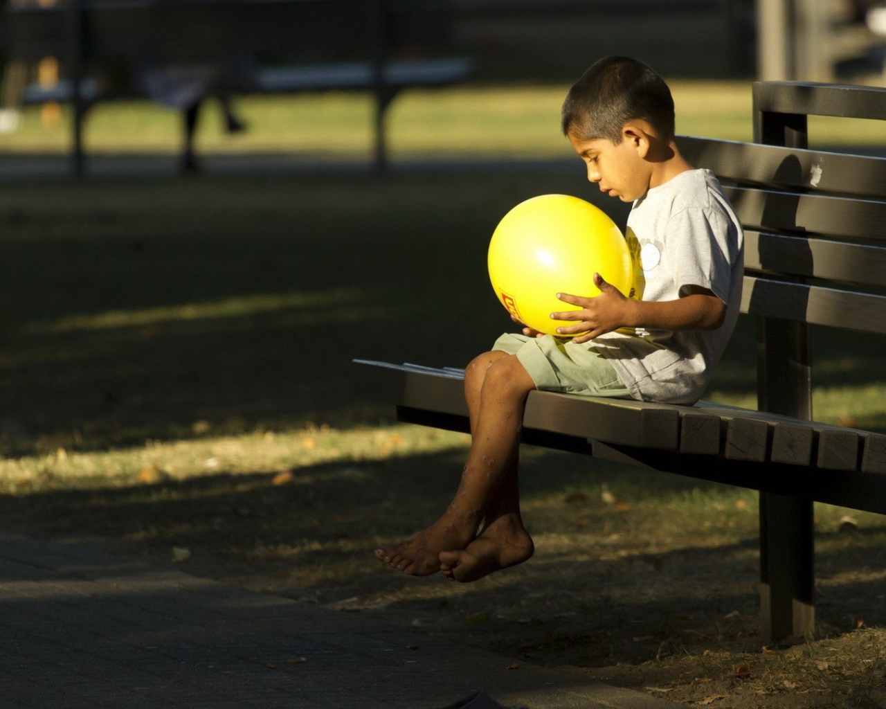 Мальчик сидит на скамье с шариком в руках