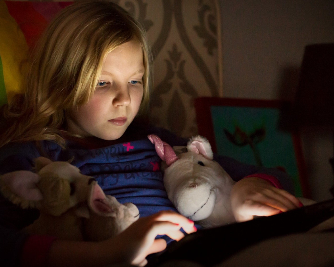 Девочка играет с планшетом лежа в кровати