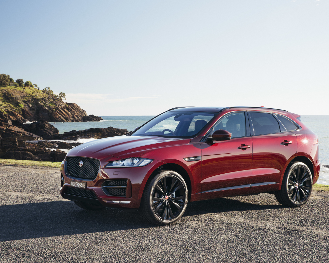 Бордовый автомобиль Jaguar F-Pace на фоне океана