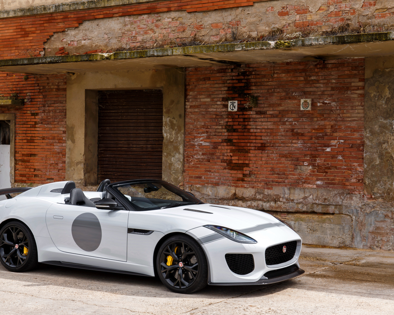 Белый автомобиль Jaguar F-Type у красной кирпичной стены