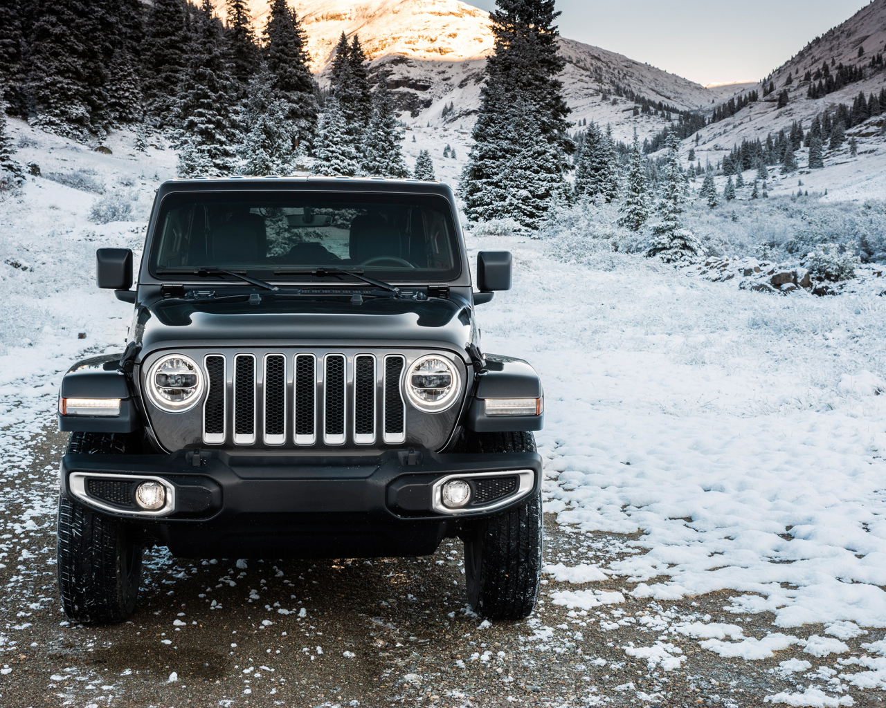 Внедорожник Jeep Wrangler Unlimited Sahara, 2018 на заснеженной дороге на фоне гор