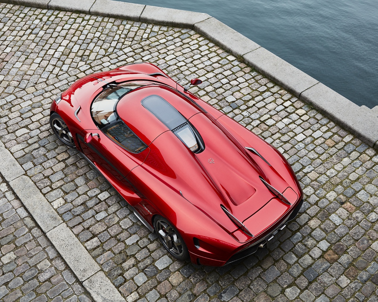 Красный спортивный автомобиль Koenigsegg Regera у воды, вид сверху