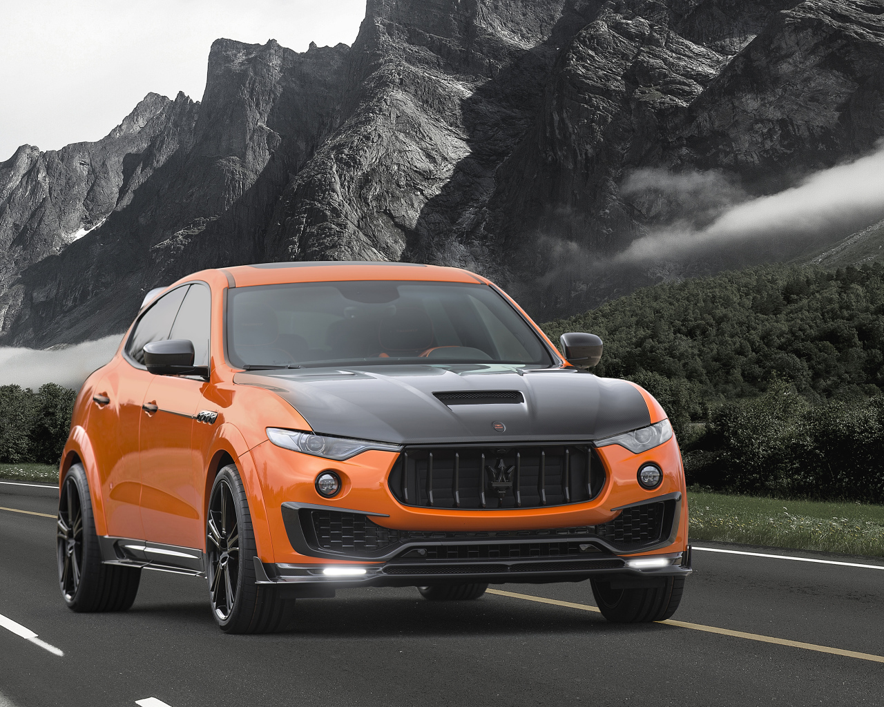 Оранжевый автомобиль Maserati Mansory Levante, 2017 на фоне гор