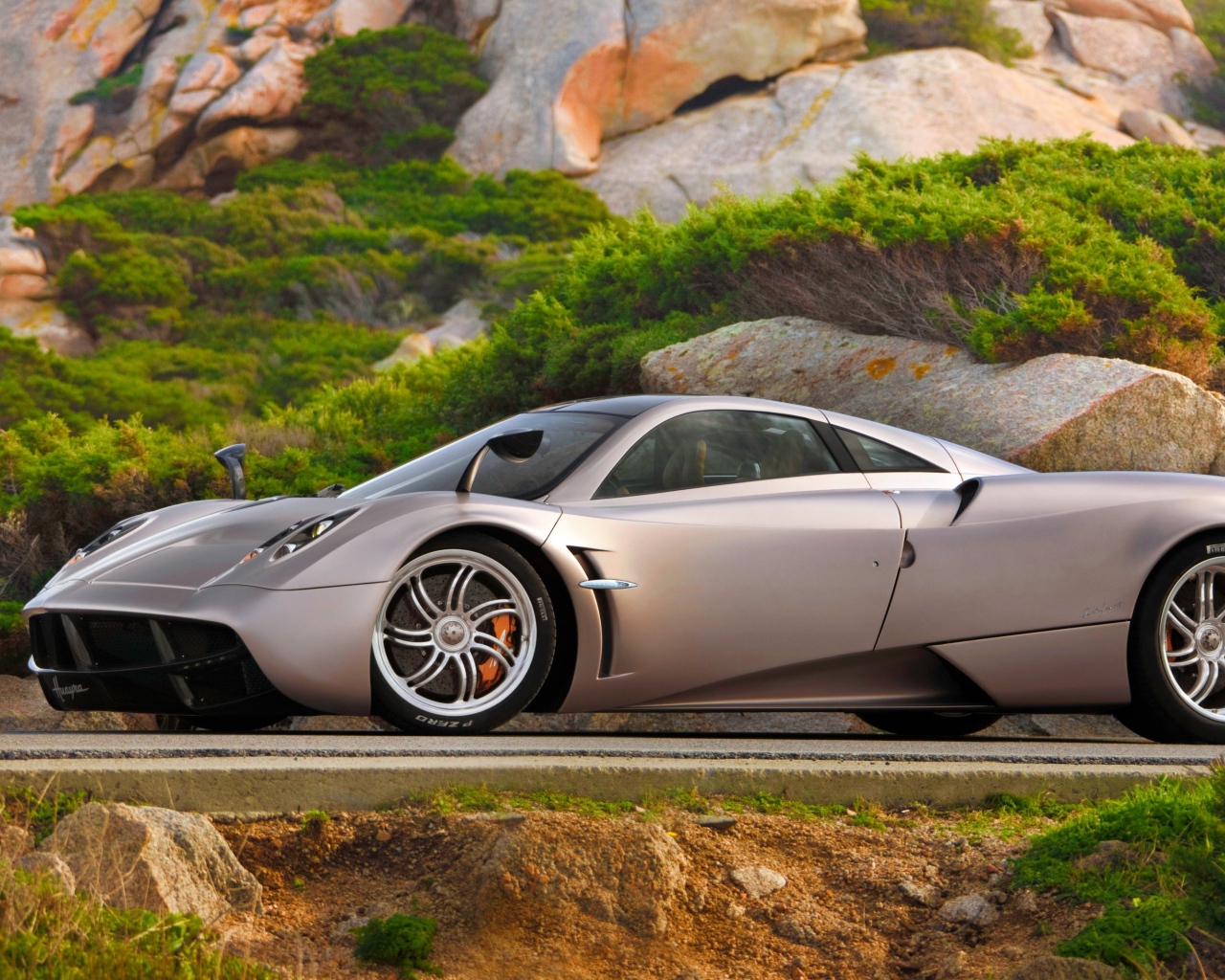Серебристый быстрый автомобиль  Pagani Huayra на трассе у скалы