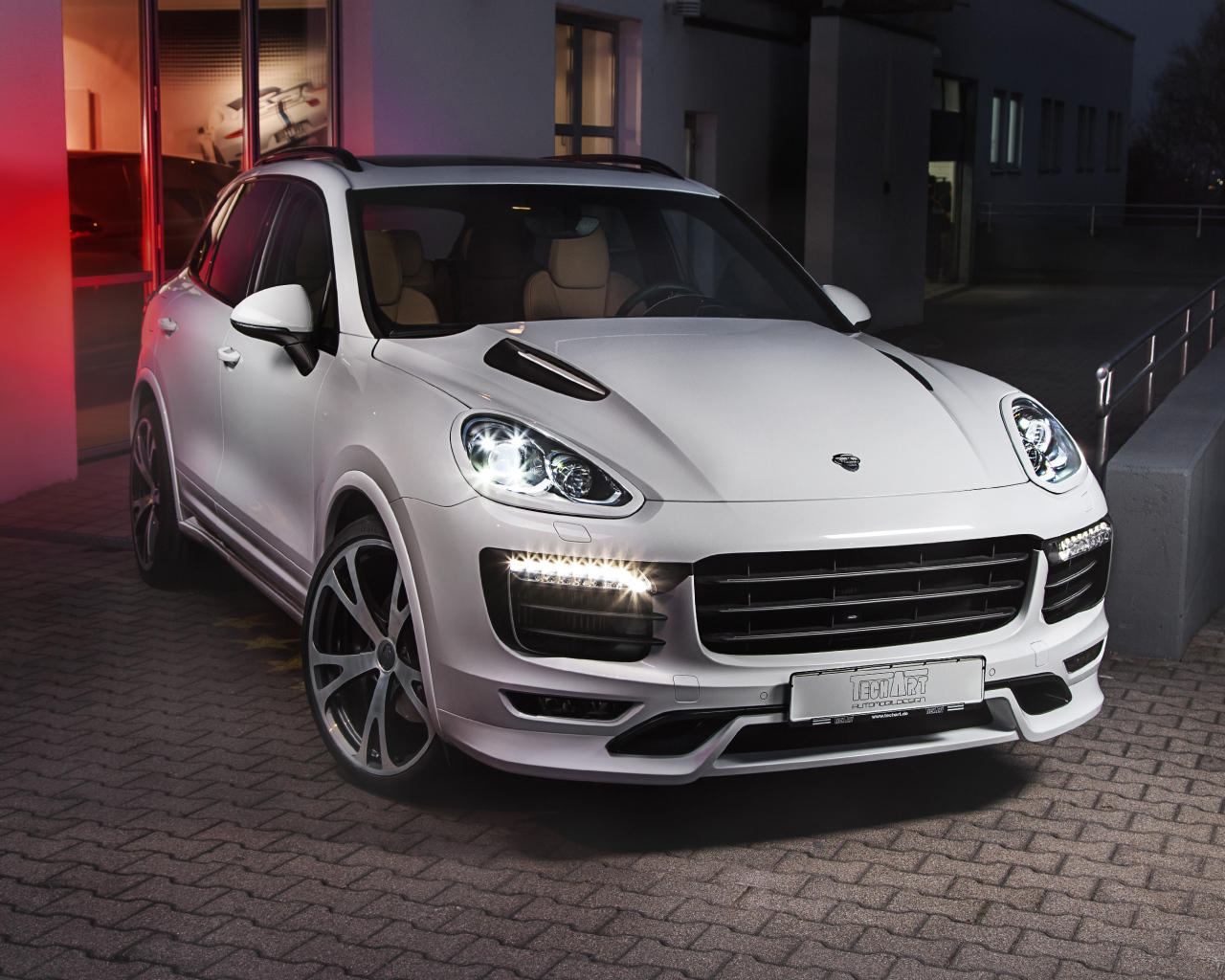 Белый внедорожник Porsche Cayenne с включенными фарами