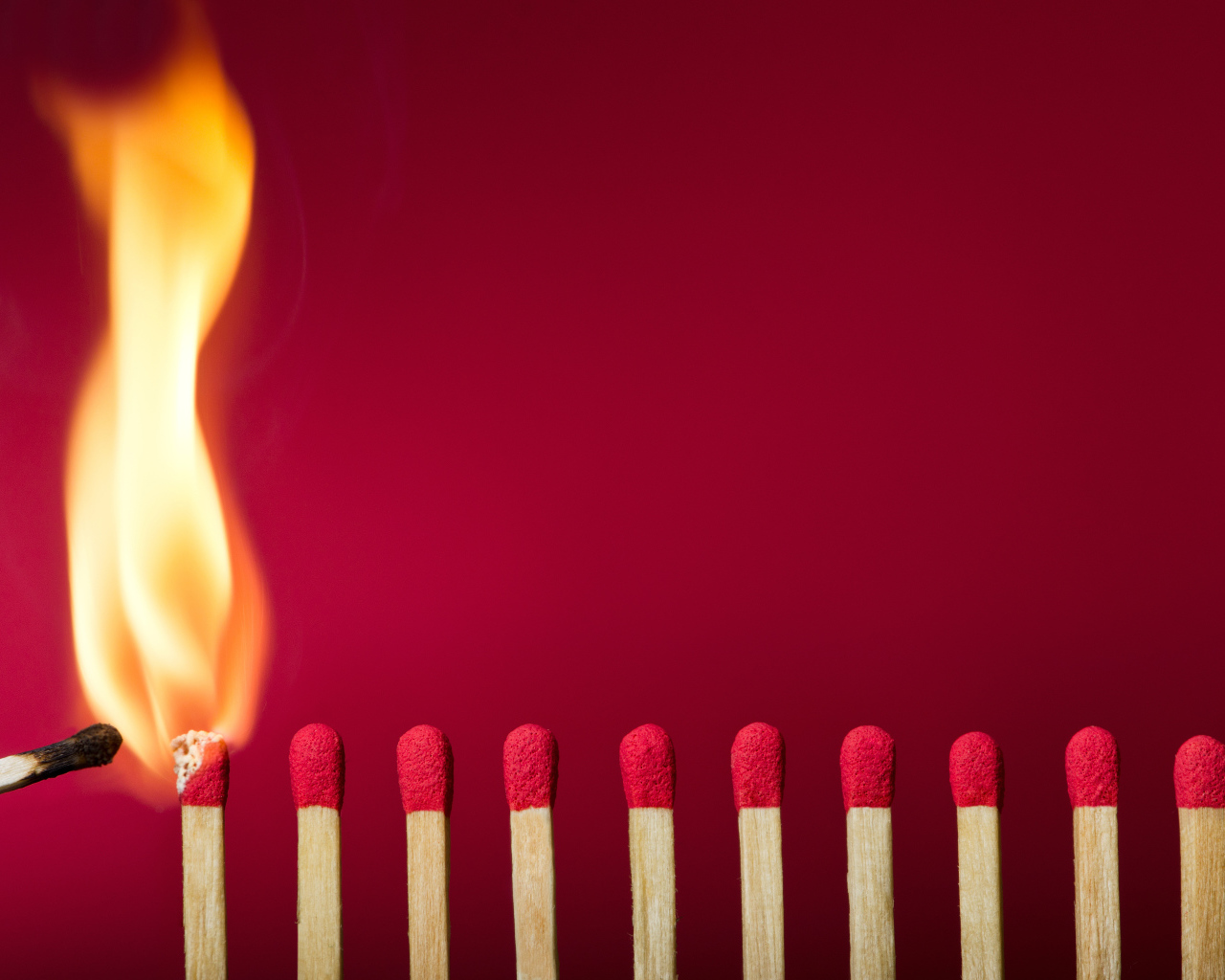 Зажженная спичка и спички на красном фоне