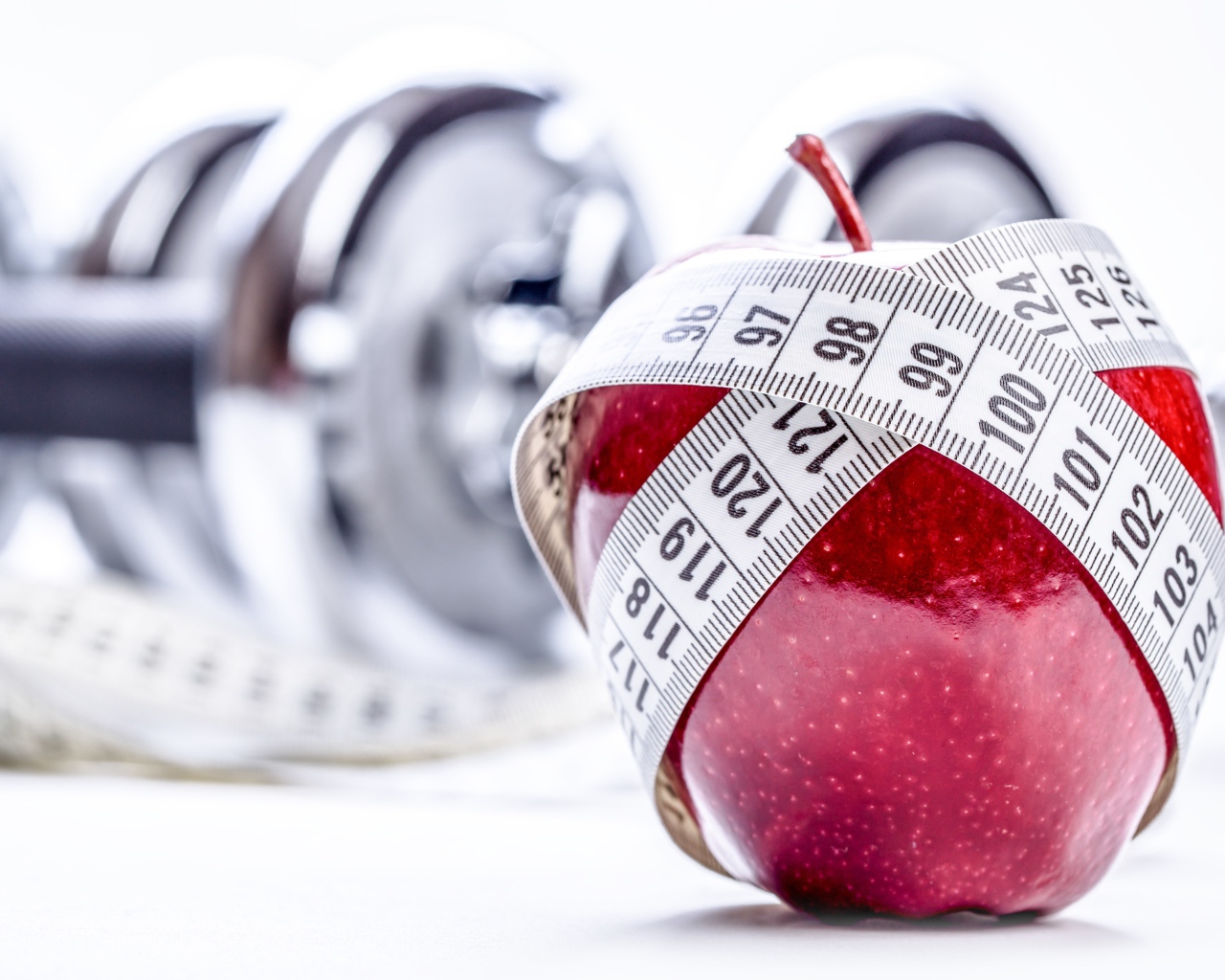 Красное яблоко перемотано мерной лентой и гантели на белом фоне
