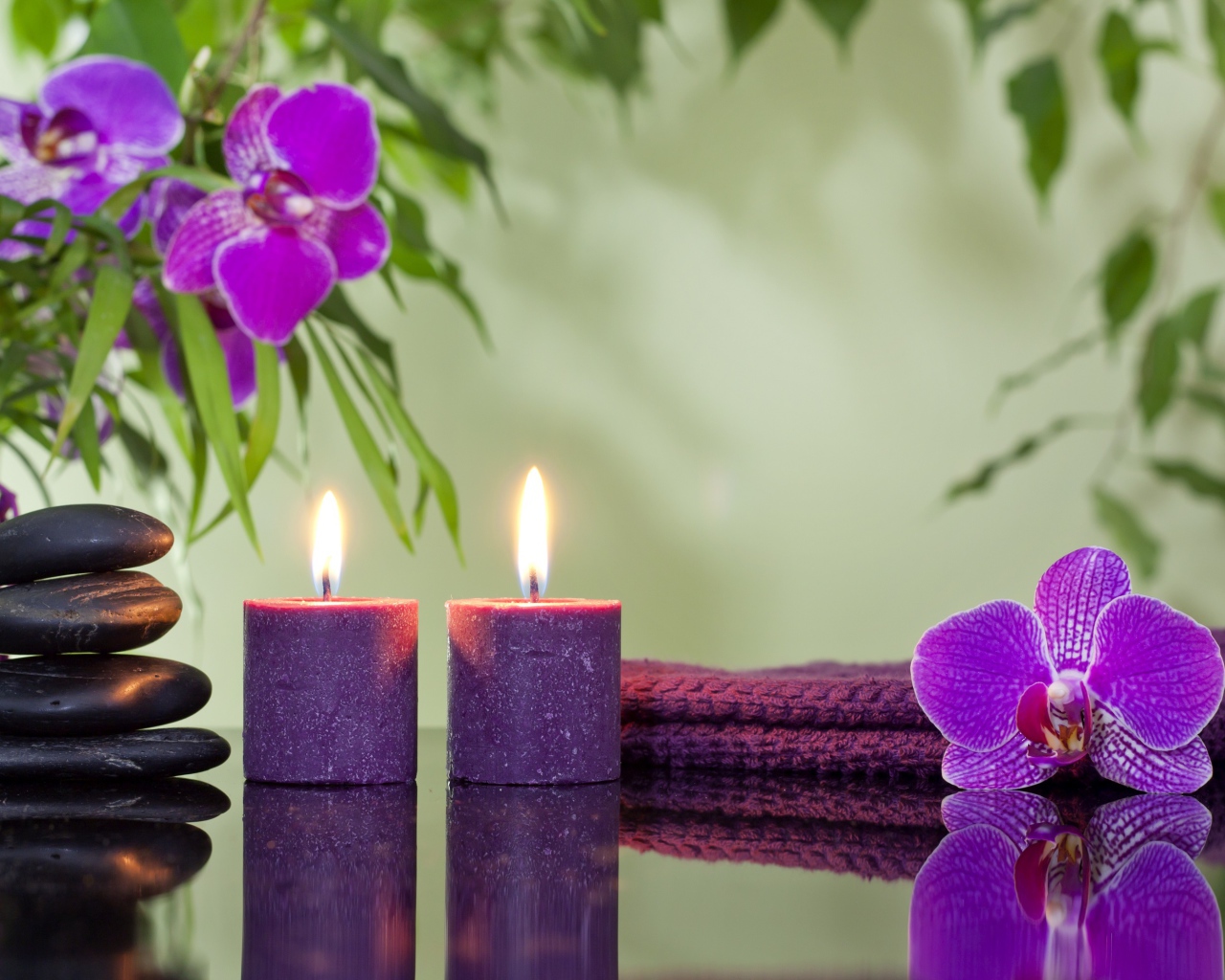 Две горящие свечи с камнями и цветами орхидеи отражаются в зеркальной поверхности стола