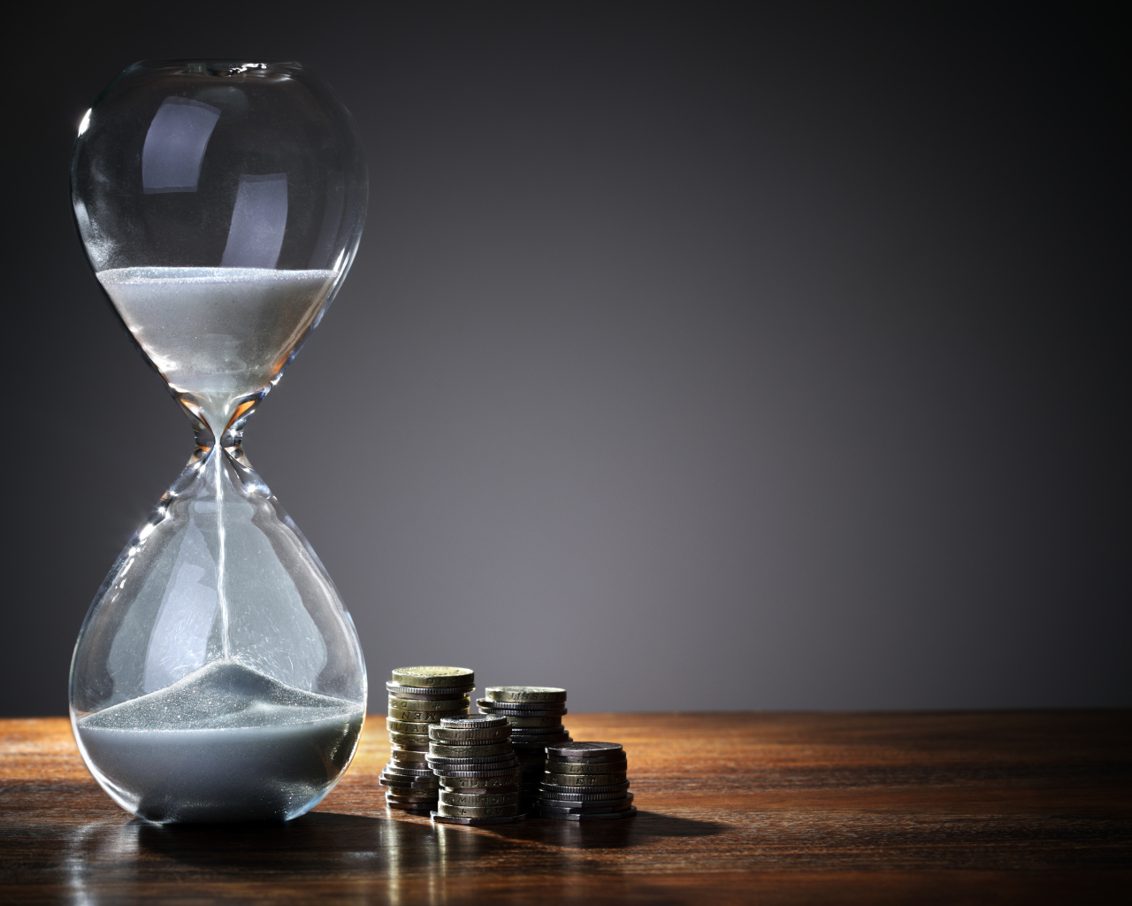 Монеты и песочные часы на столе