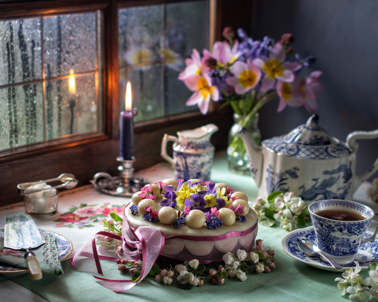 Красивый торт на столе с сервизом и горящей свечой у окна