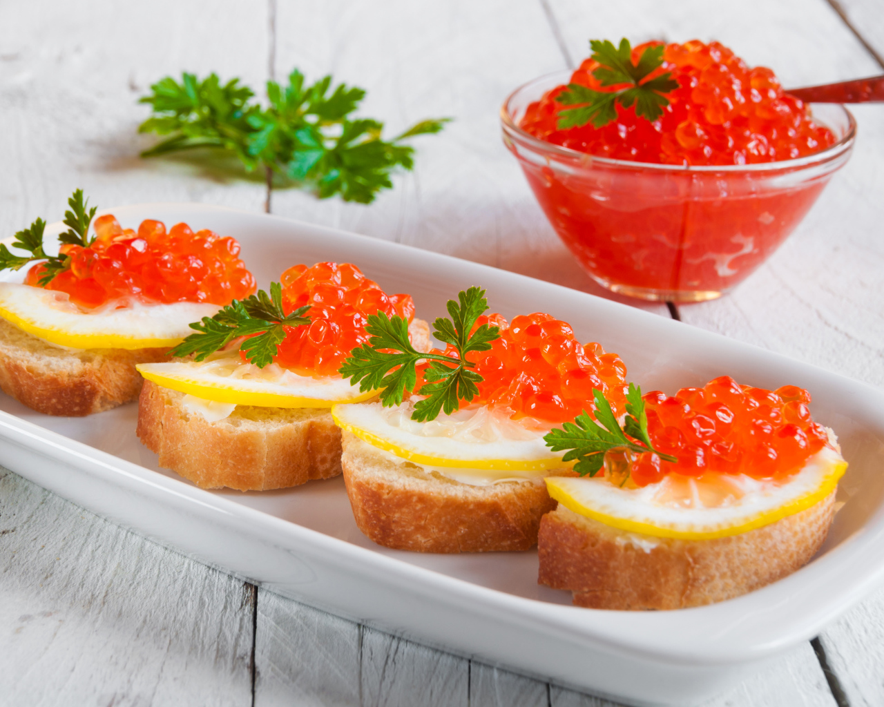 Бутырброды с красной икрой и лимонами на белой тарелке