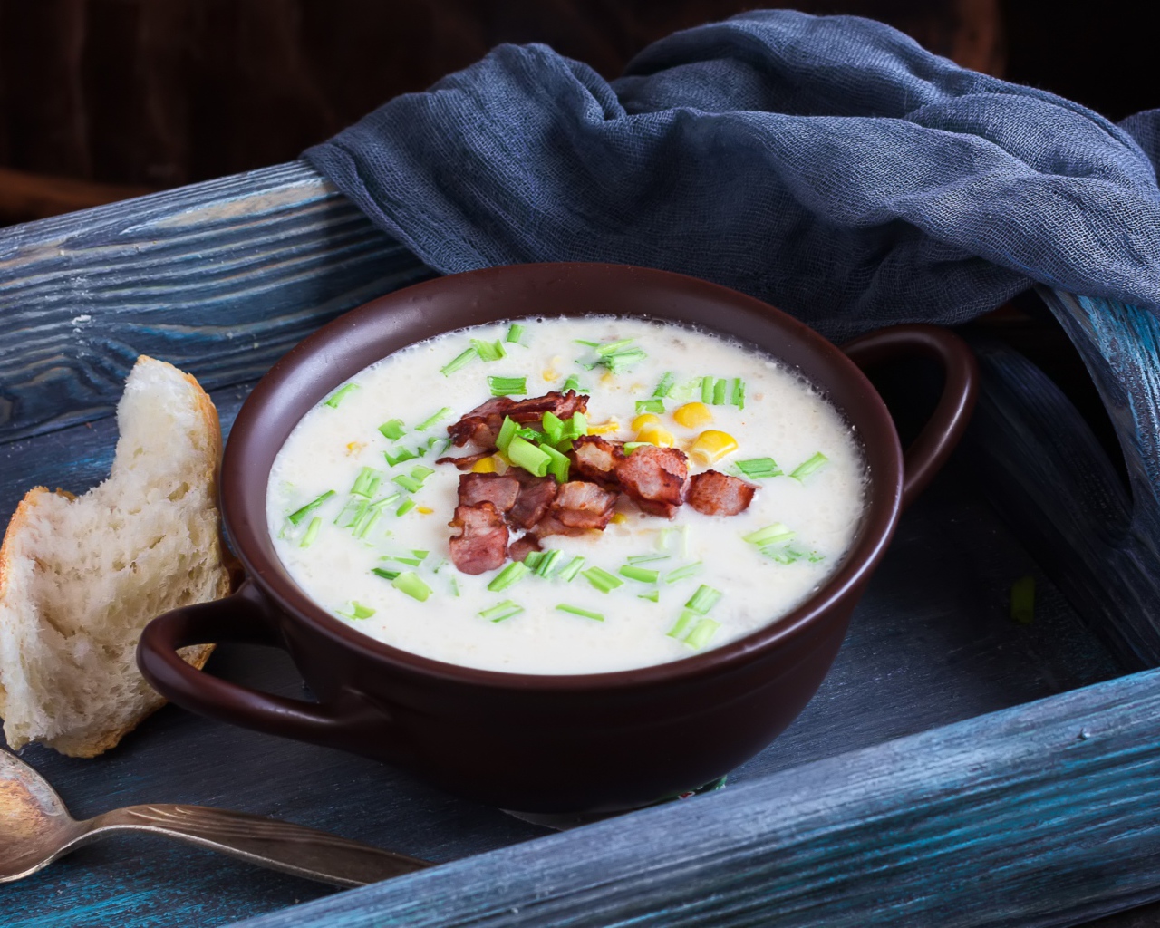 Сырный суп с зеленью и беконом на столе с куском хлеба
