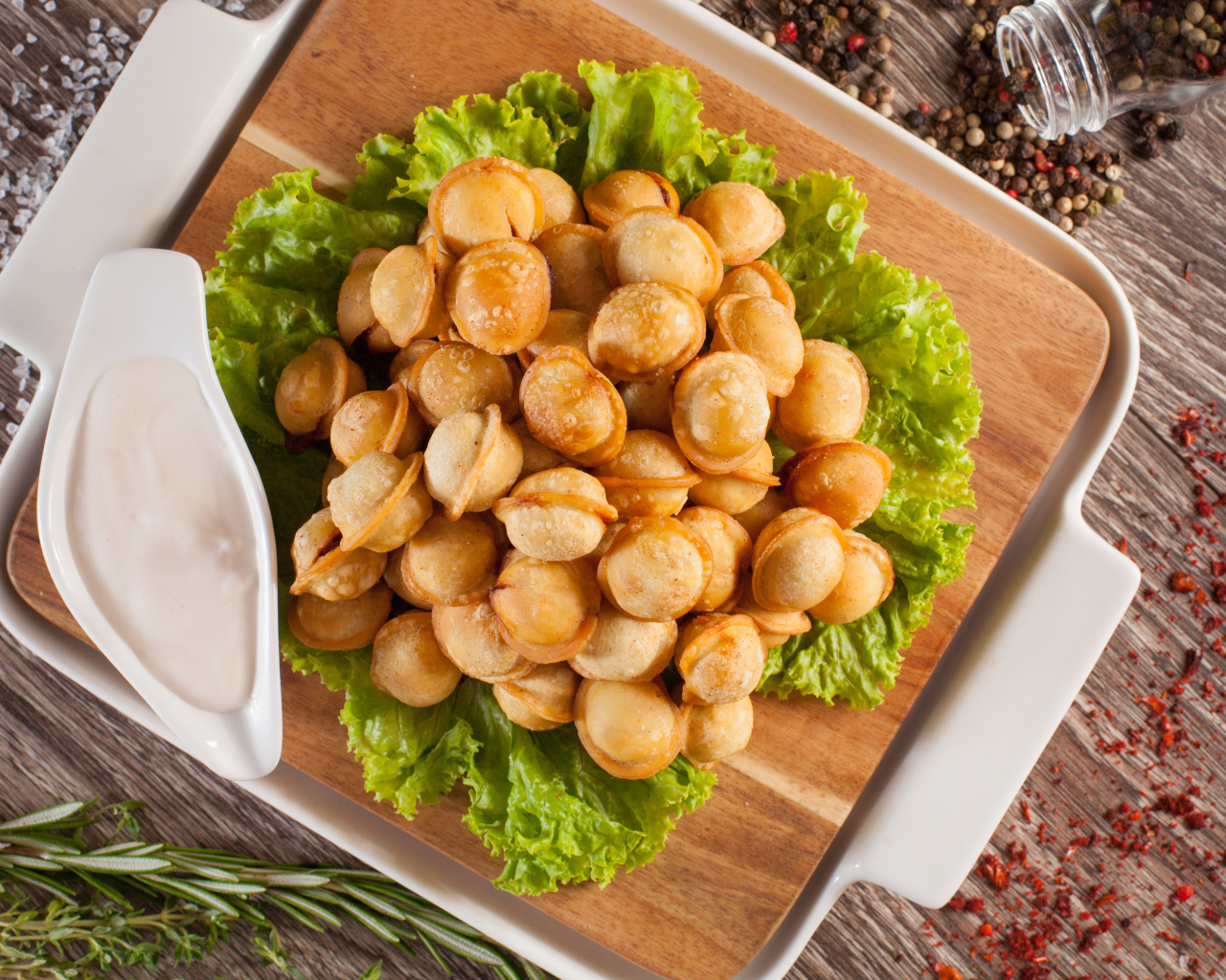 Пельмени с соусом и листьями салата лежат на разделочной доске