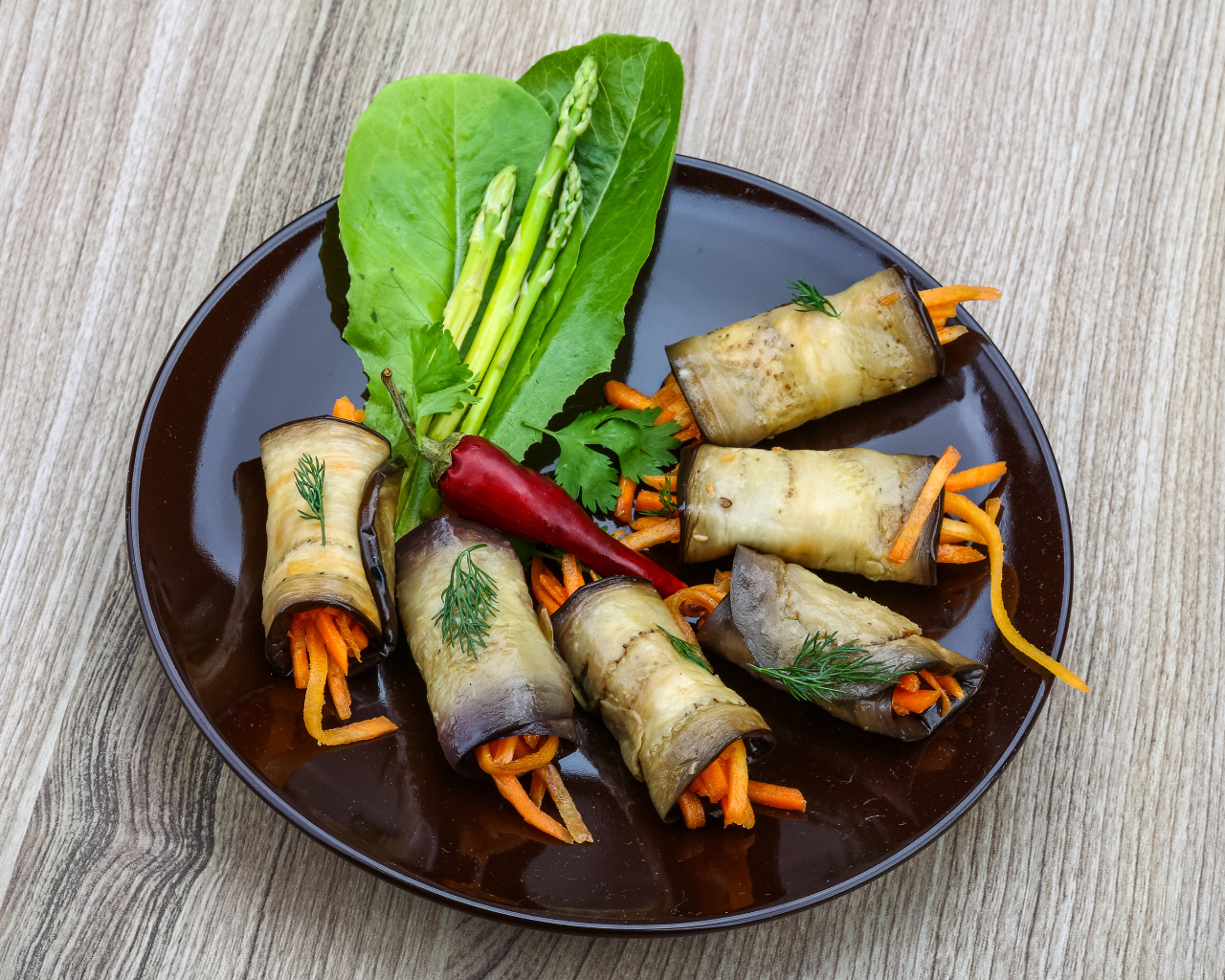 Рулетики из баклажанов с морковью на тарелке с листьями салата