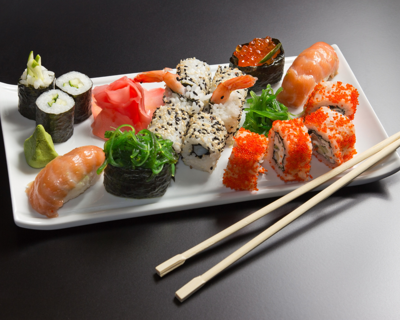 Суши и роллы на белой тарелке с палочками на сером фоне