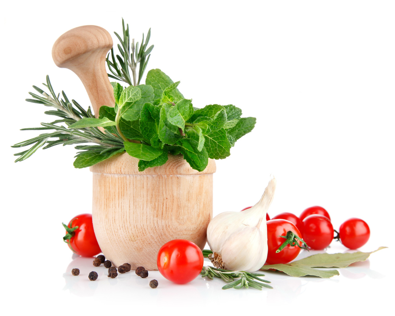 Деревянная ступа и пестик со специями и зеленью на столе с чесноком и помидорами