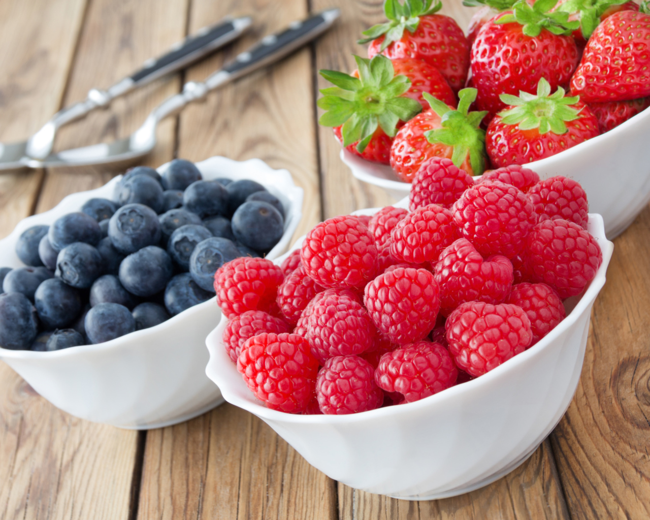 Свежие ягоды малины, клубники и черники в белых тарелках на столе