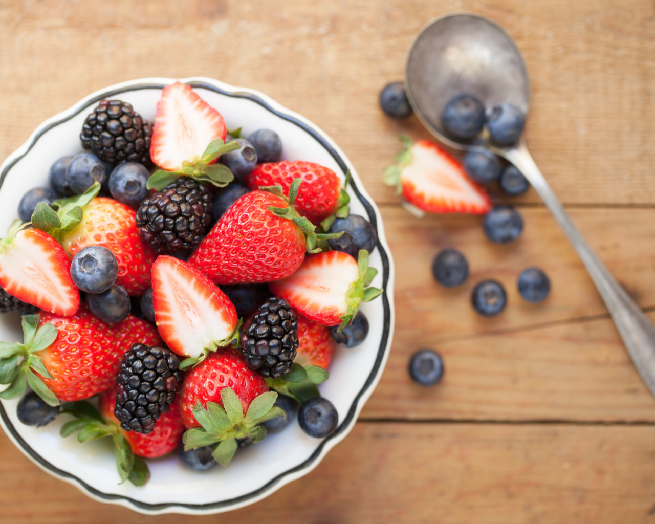 Свежие ягоды клубники, черники и ежевики в тарелке на деревянном столе