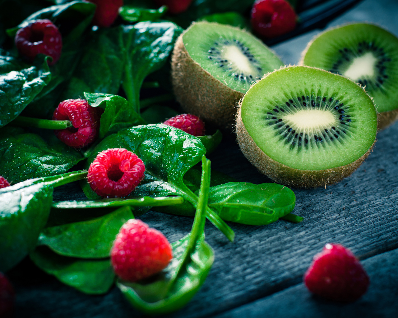 Половинки киви на столе с зелеными листьями и свежей малиной