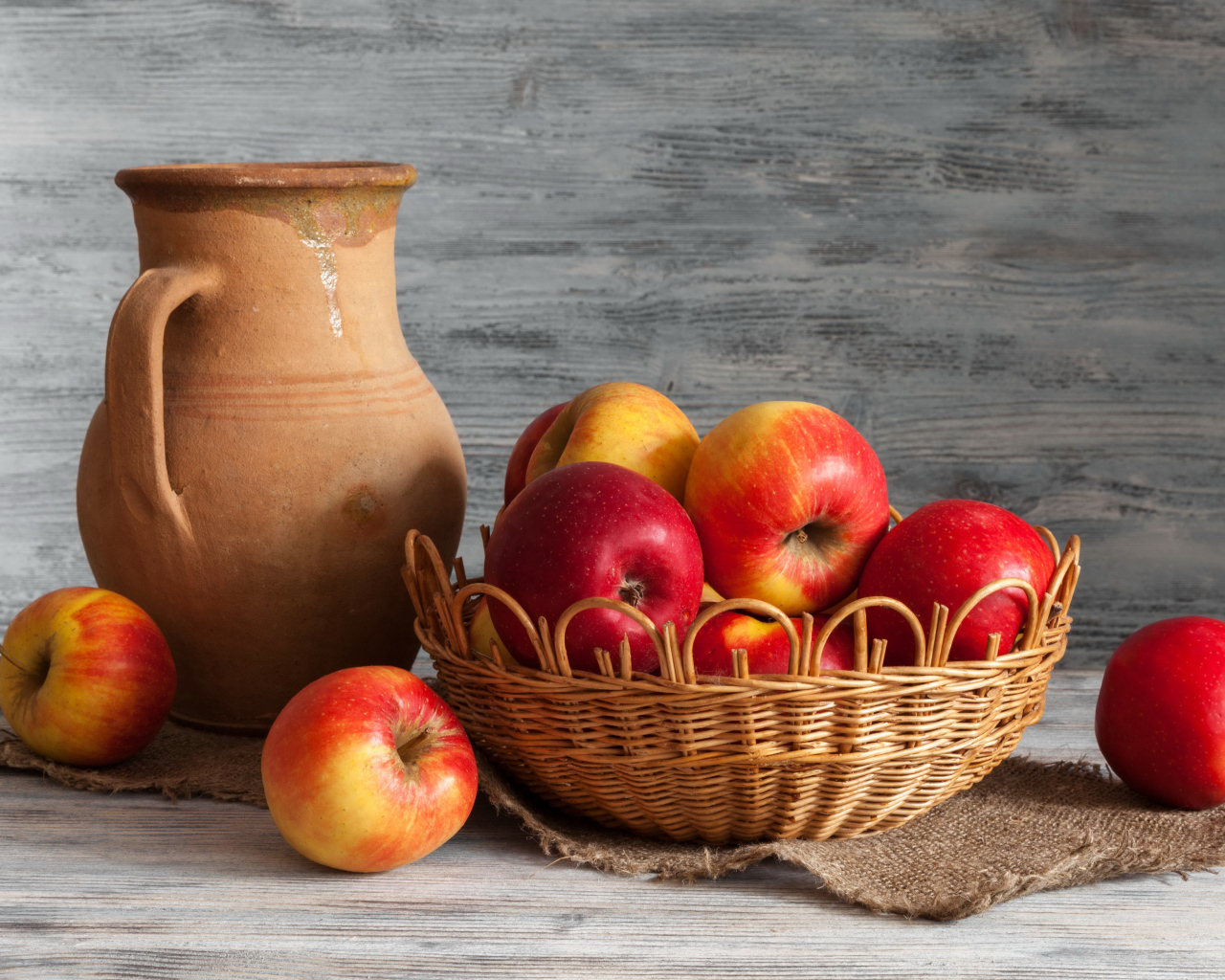 Красные яблоки в корзинке на столе с кувшином