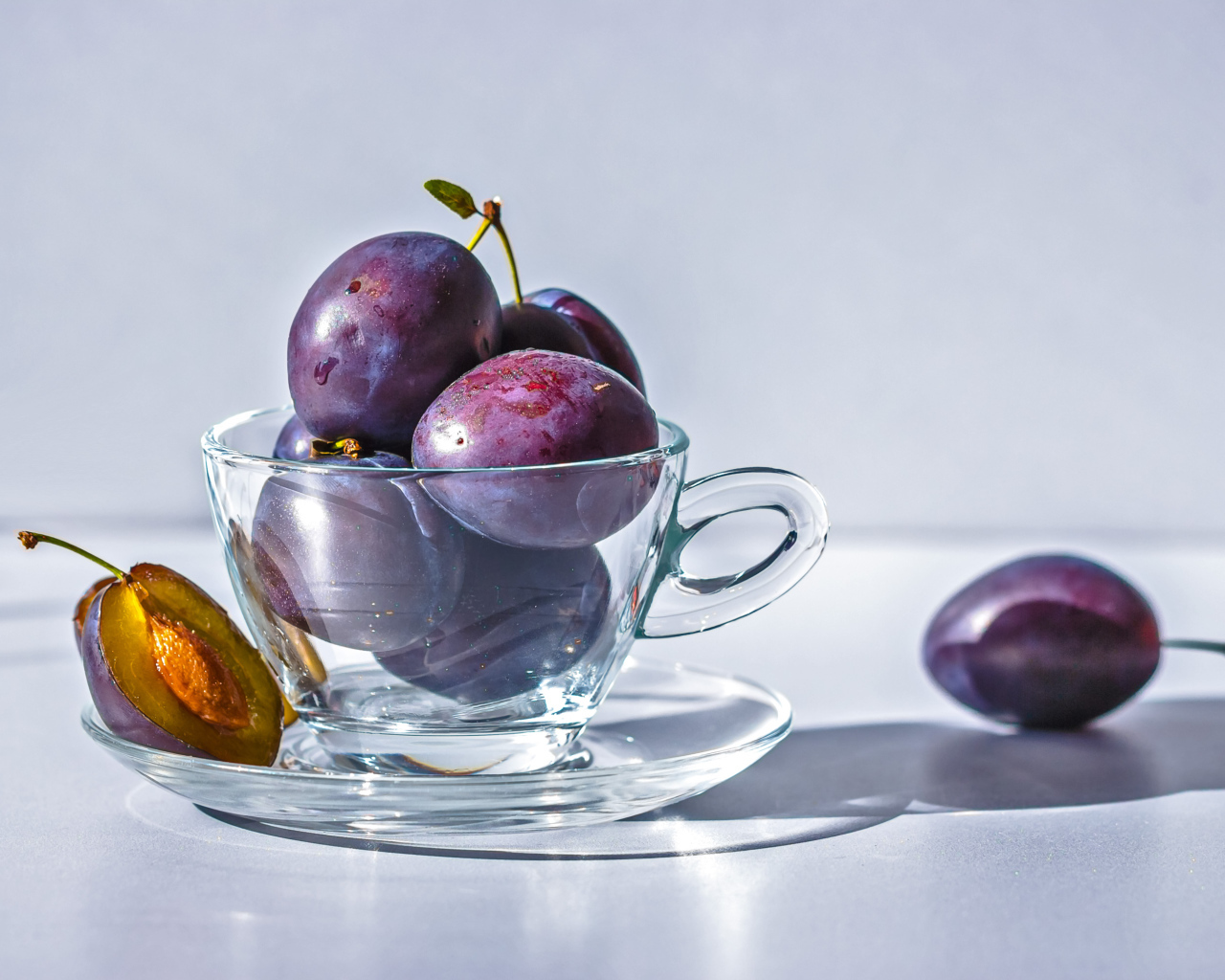 Спелые синие сливы на столе в стеклянной чашке