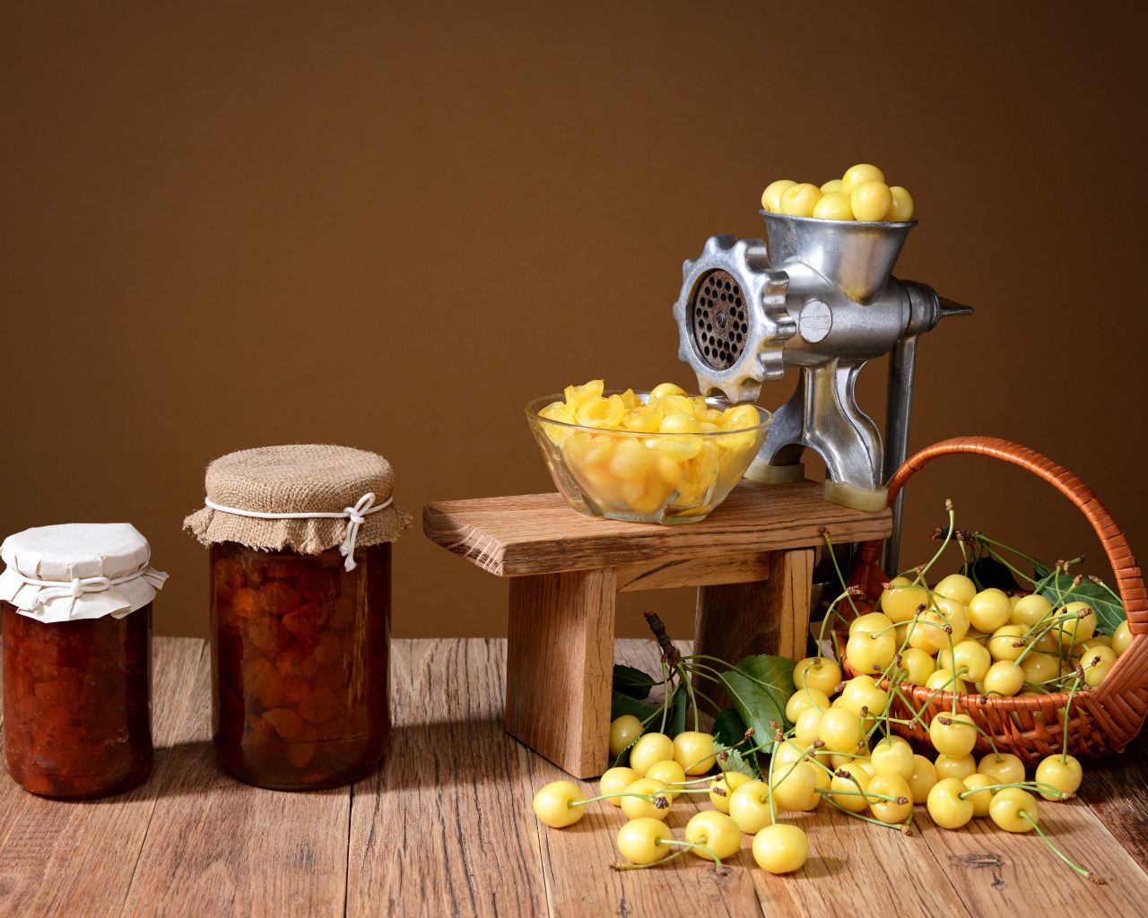Две баночки варенья и желтые черешни на столе с мясорубкой