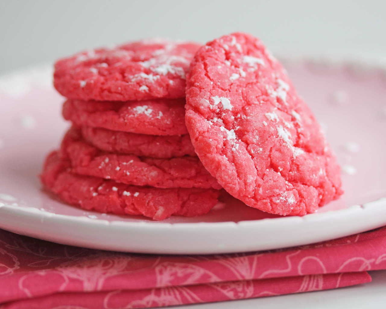 Печенье розового цвета на белой тарелке с сахарной пудрой