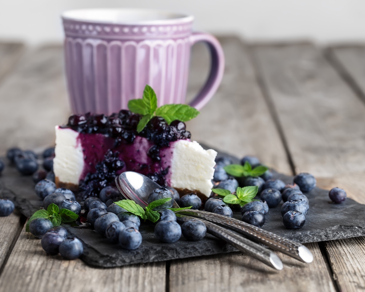Черничный чизкейк со свежими ягодами лежит на столе с чашкой