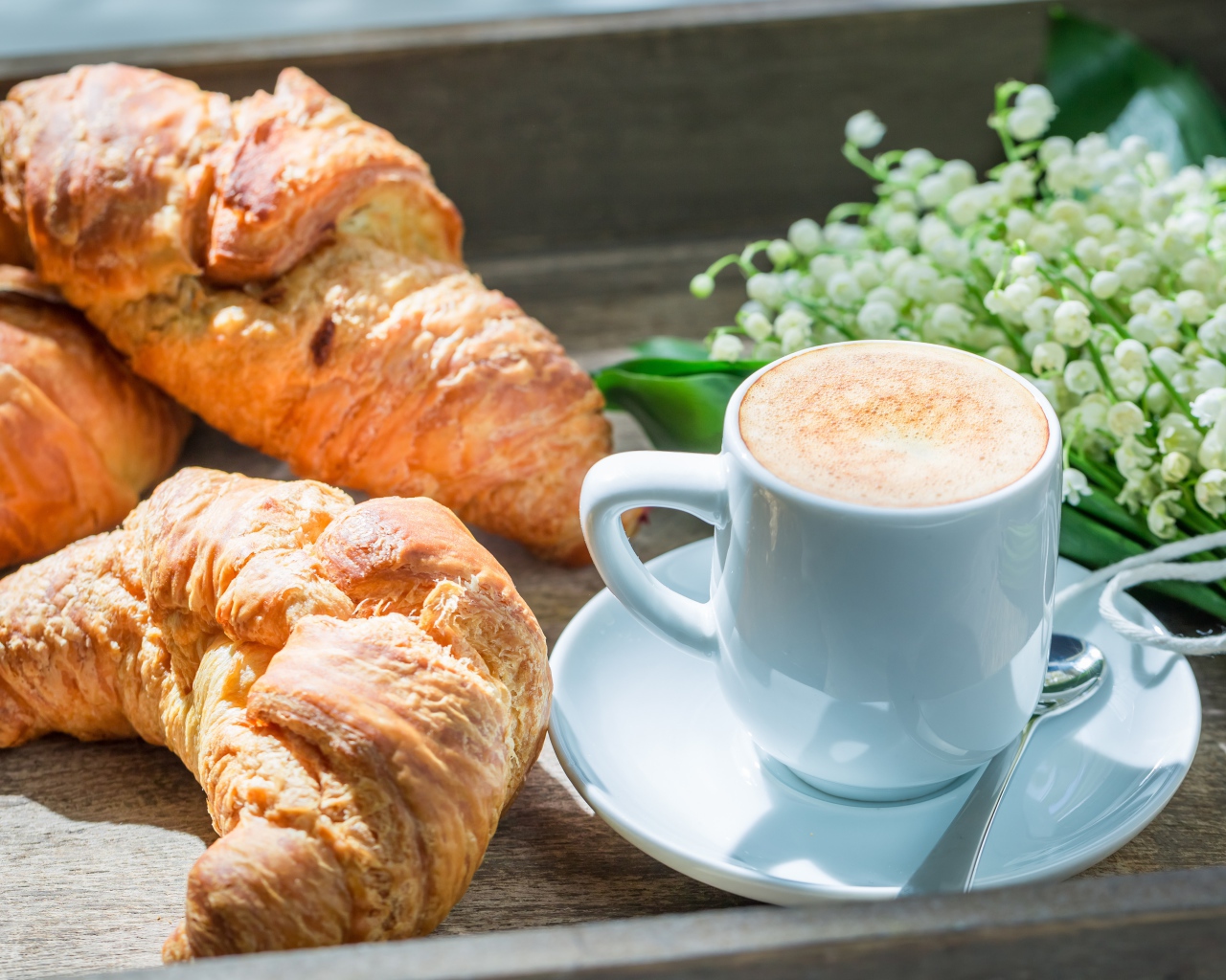 Свежие круассаны с чашкой кофе и букетом ландышей на столе