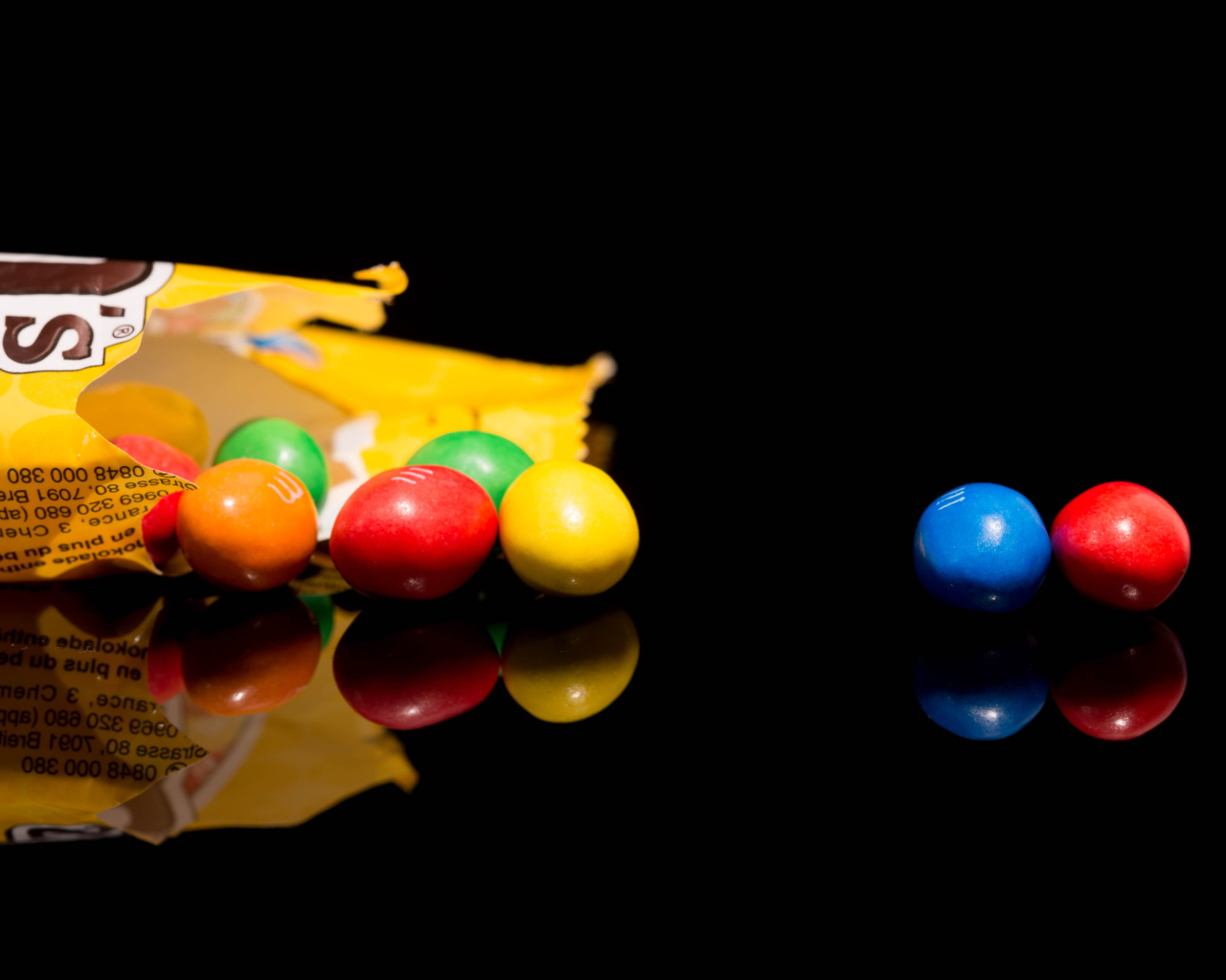 Разноцветные конфеты  M&m's отражаются в черной поверхности стола 