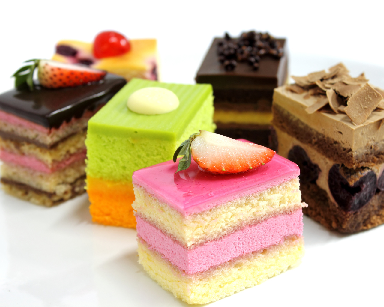 Разноцветные пирожные с ягодами на белом фоне