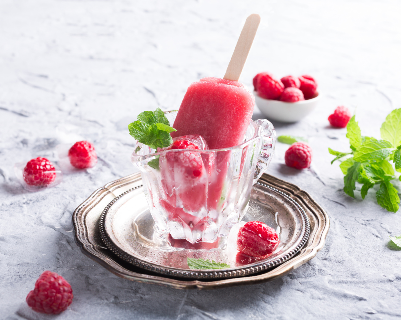 Малиновое мороженое на палочке в стеклянном стакане на столе со свежими ягодами