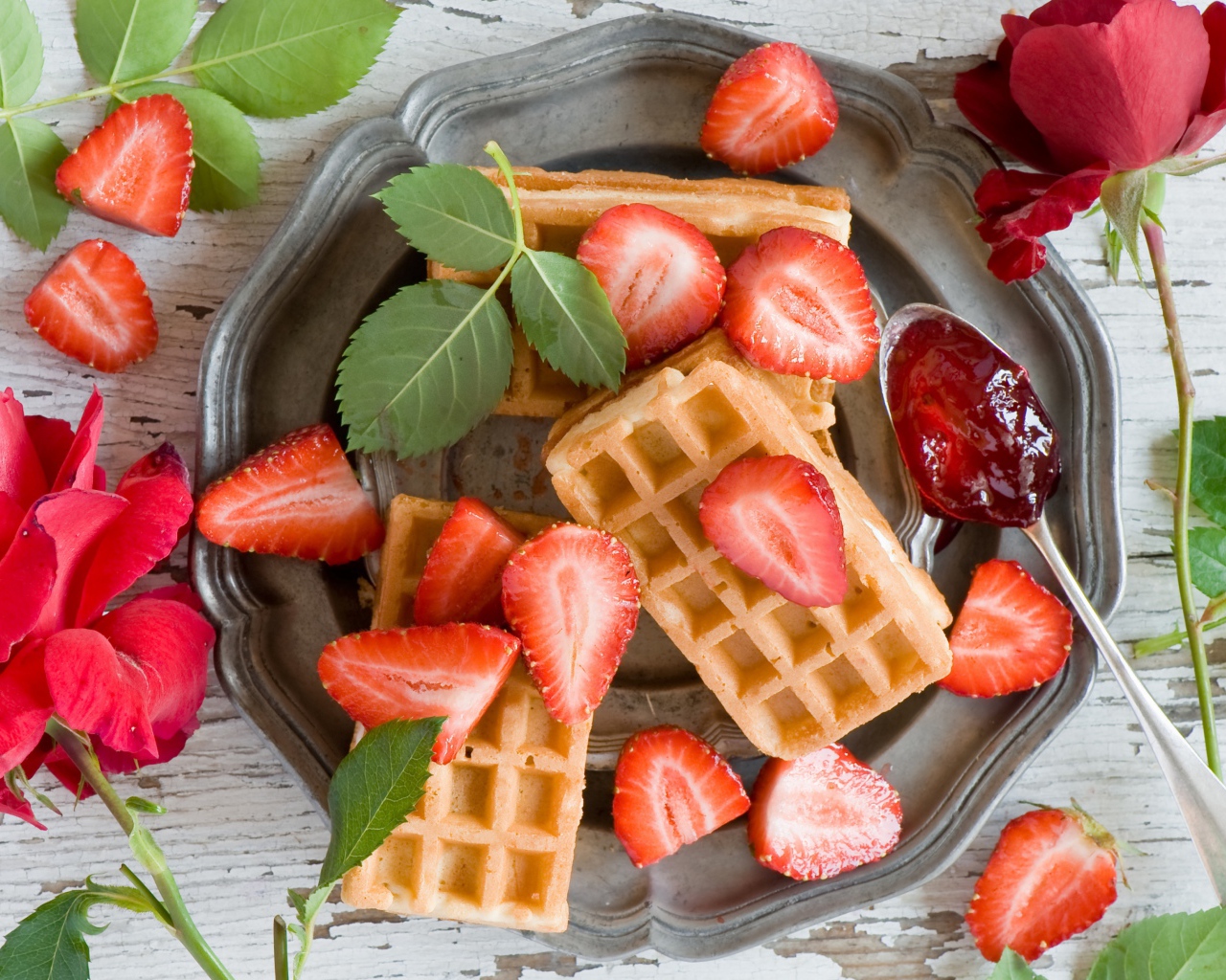 Сладкие вафли со свежей клубникой и красными розами на столе