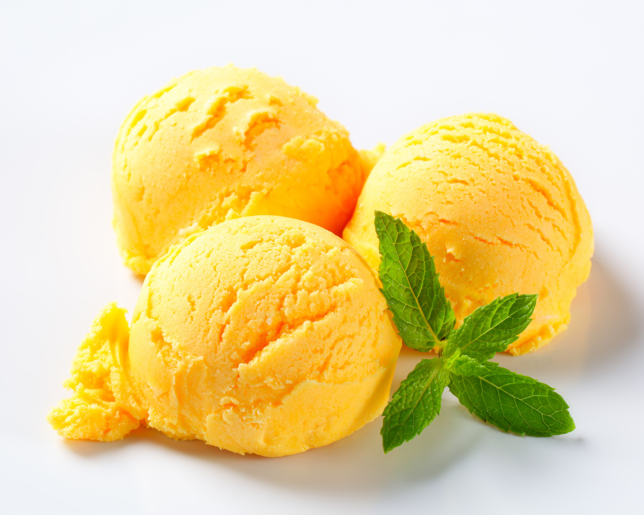 Три шарика фруктового мороженого с листиком мяты на белом фоне
