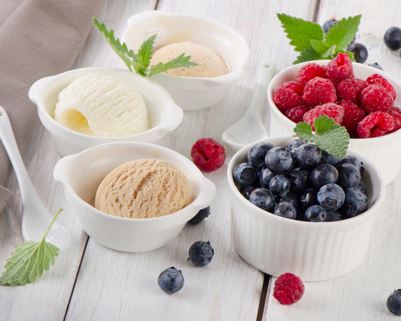 Три шарика мороженого и свежие ягоды малины и черники в белых тарелках