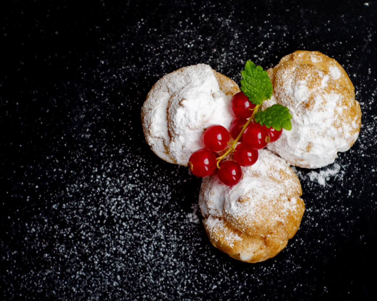 Три пирожных с сахарной пудрой и красной смородиной на черном фоне