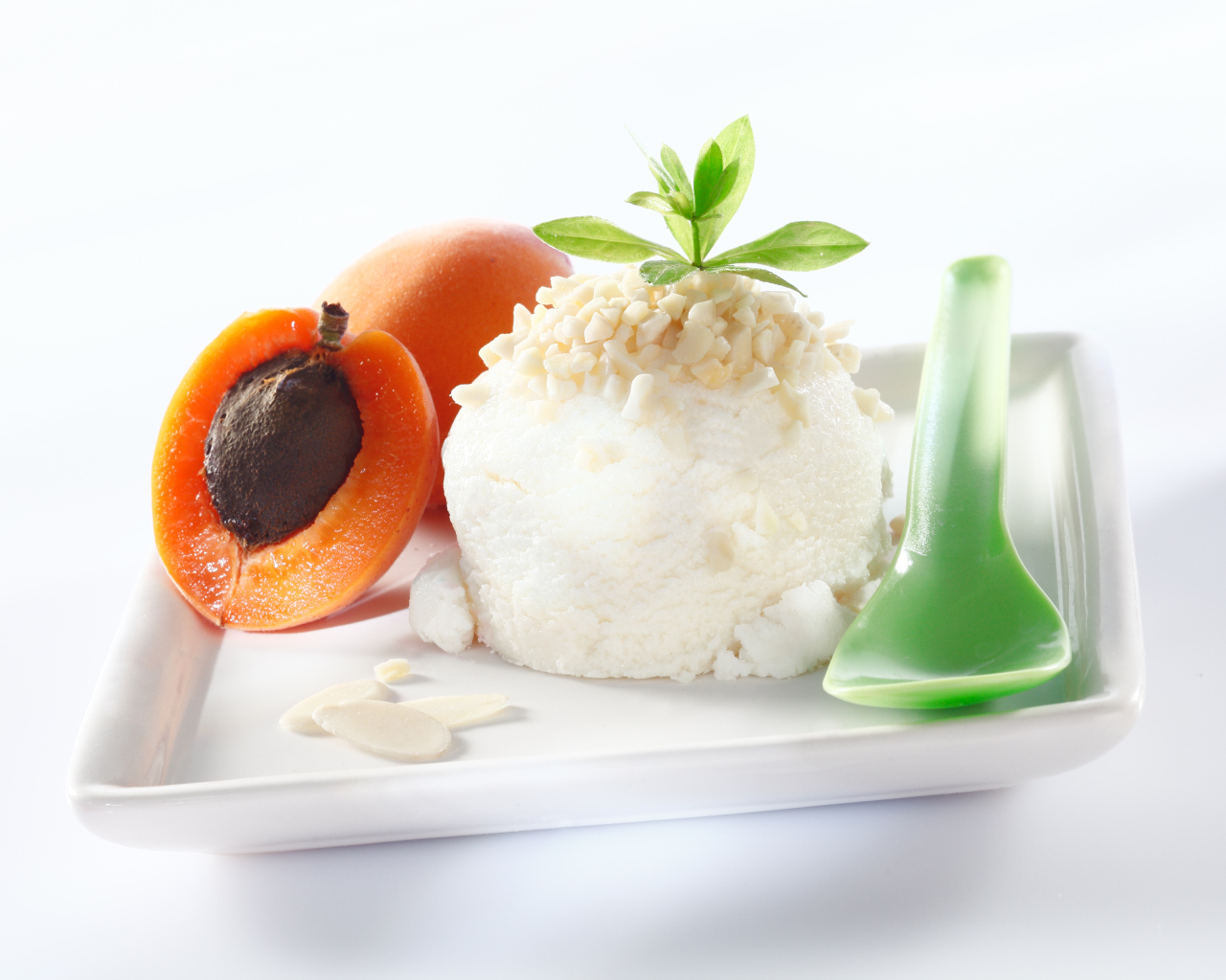 Шарик ванильного мороженого с абрикосами на белой тарелке с ложкой