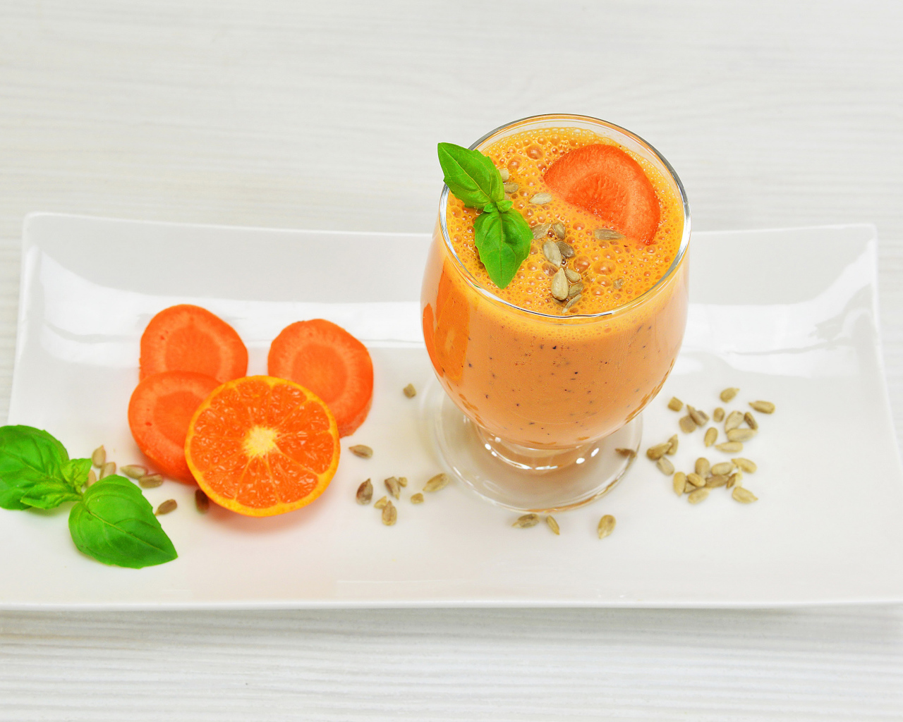 Бокал морковного коктейля с апельсином на белой тарелке