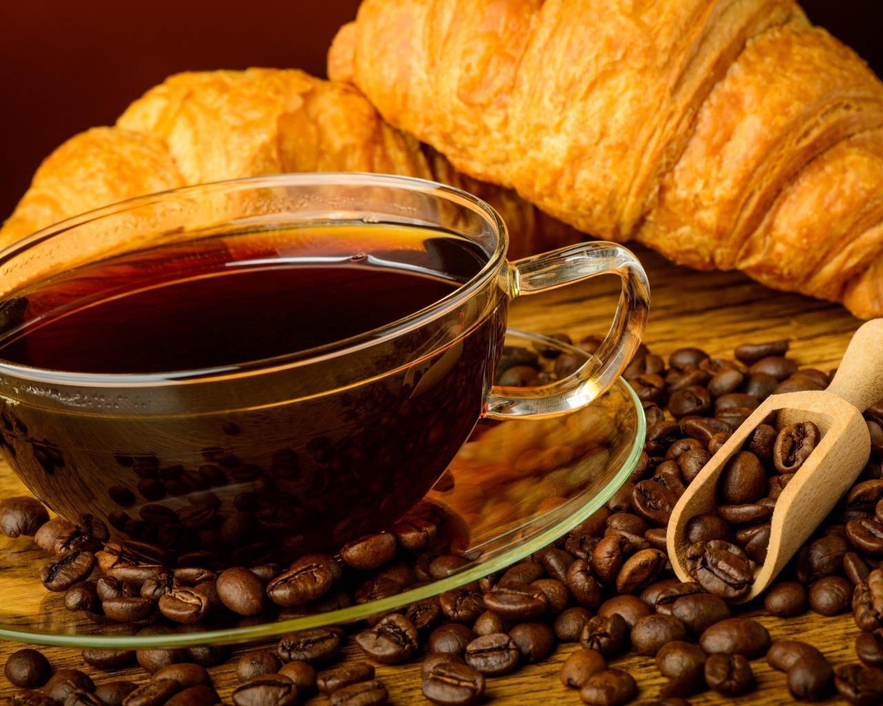 Стеклянная чашка кофе с зернами и свежими круассанами на столе