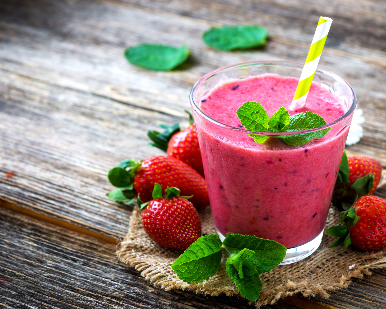 Клубничный смузи в стакане с трубочкой и свежими ягодами на столе