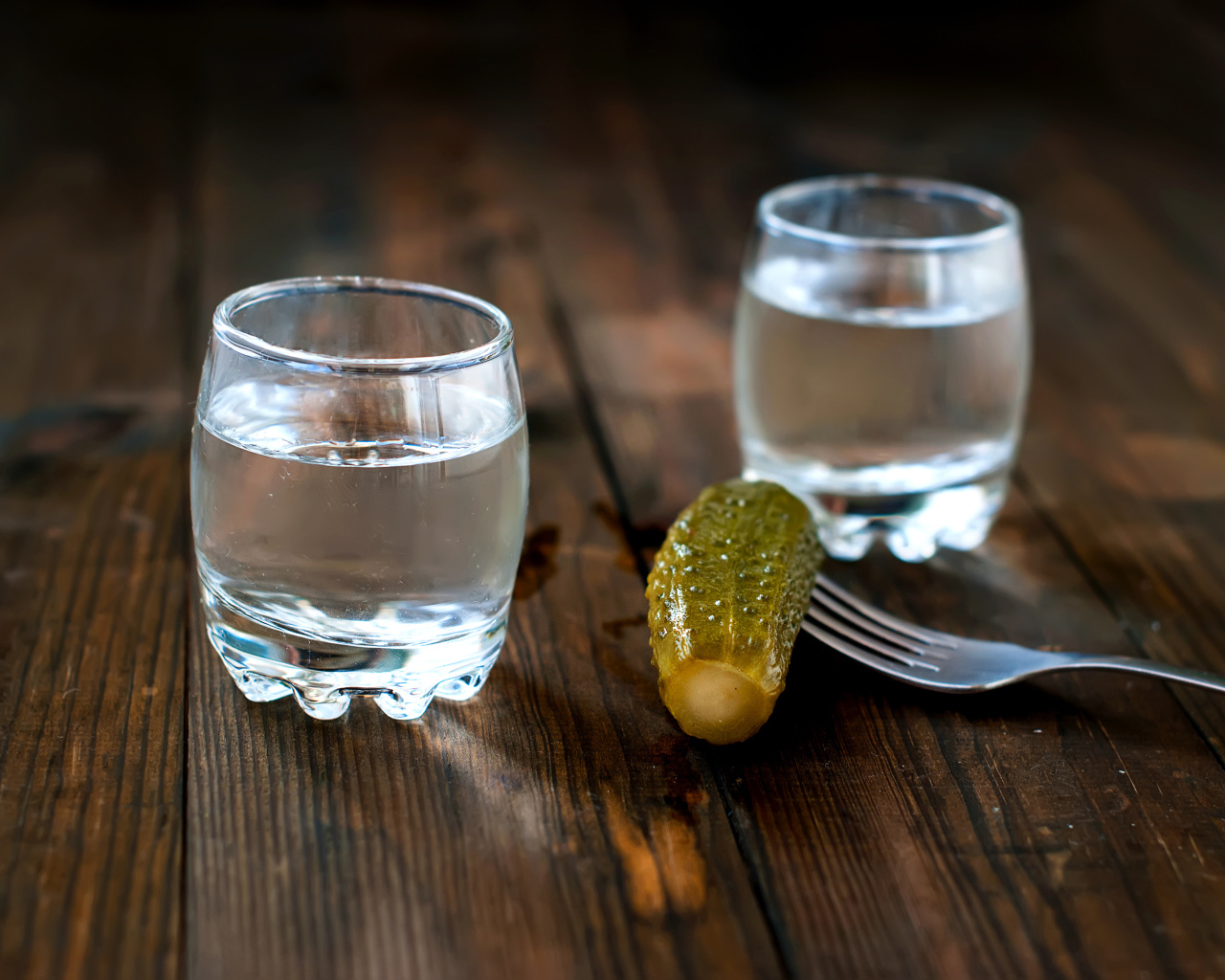 Две рюмки водки и соленый огурец на столе