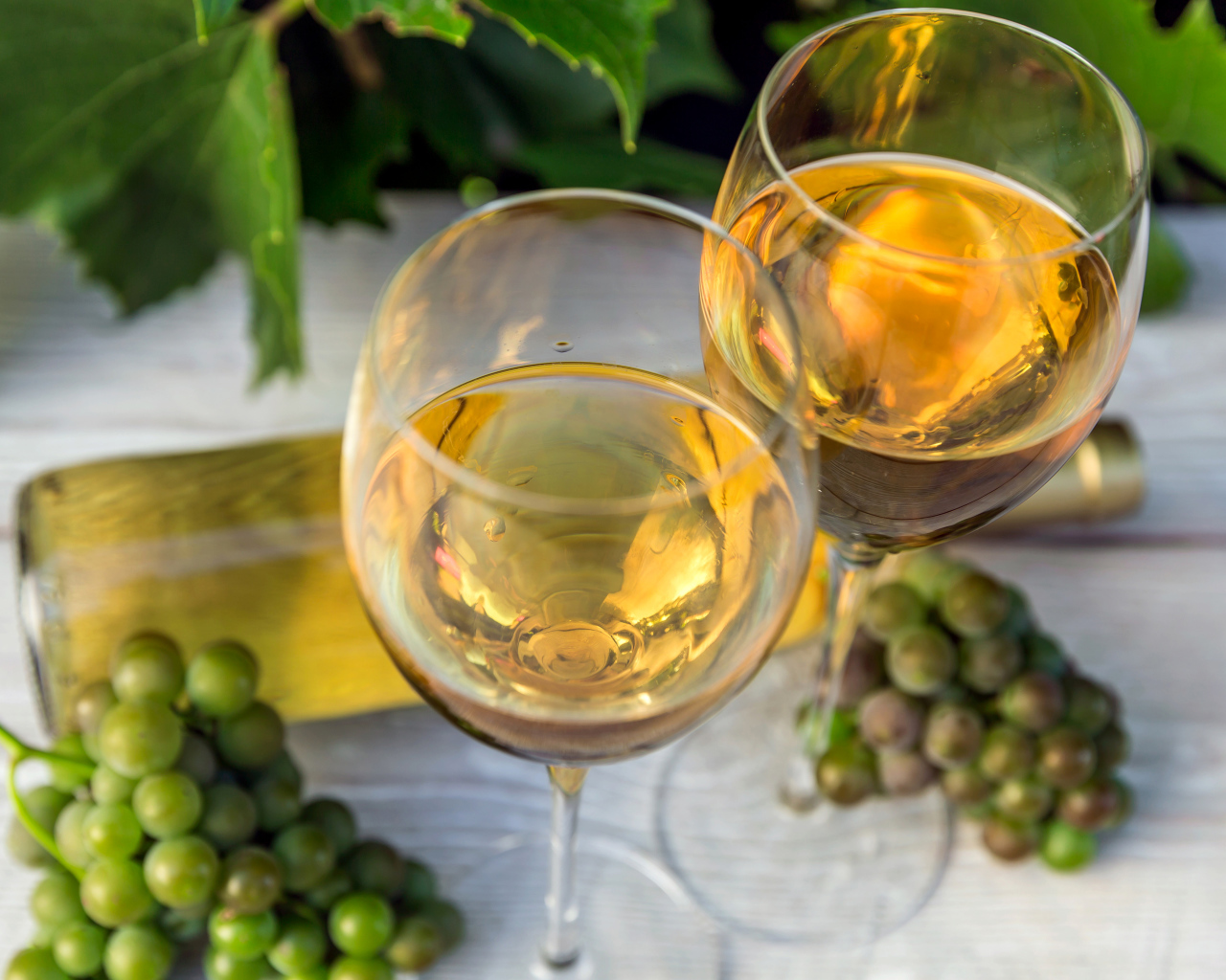 Два бокала белого вина с белым виноградом на столе
