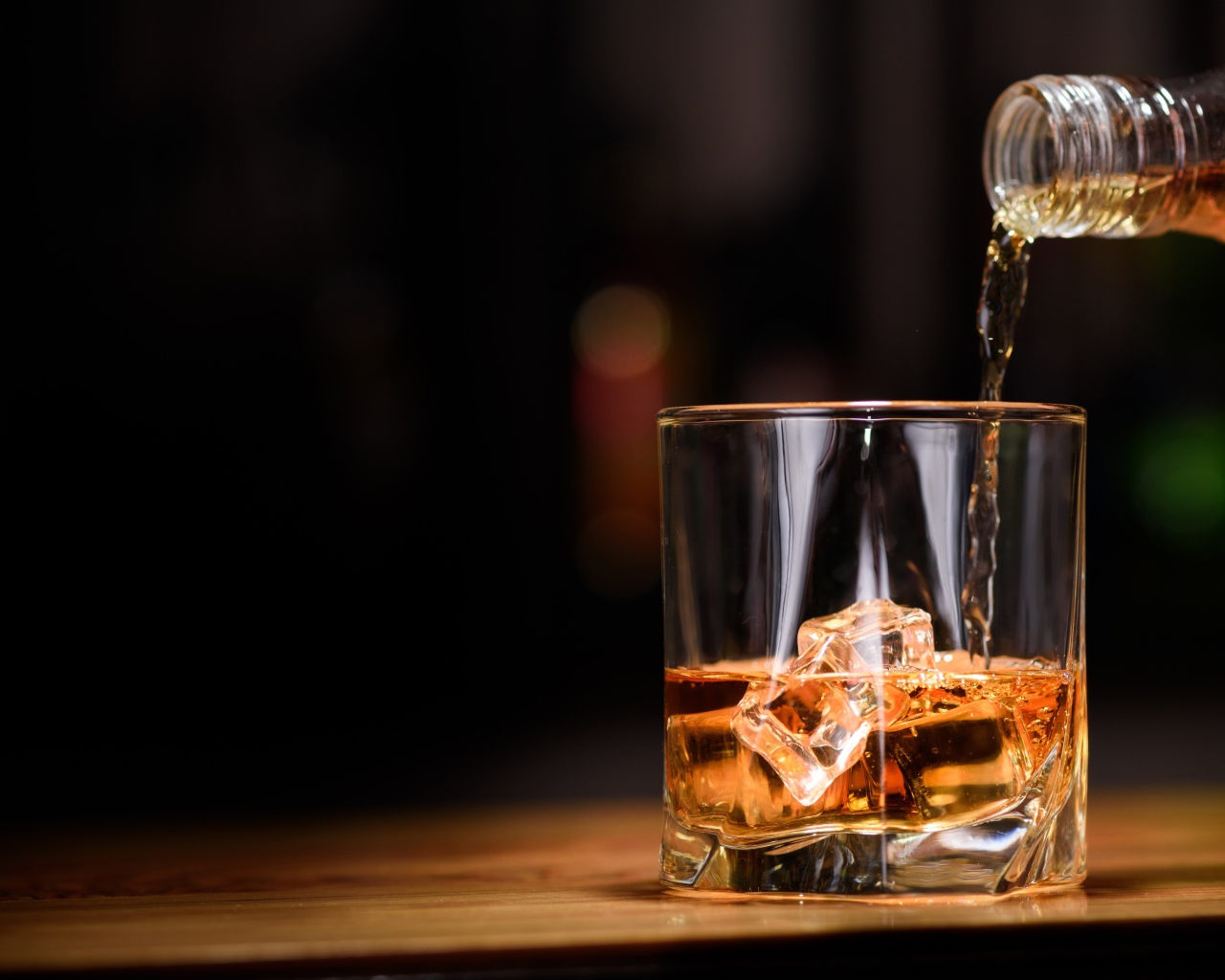 Виски наливают из бутылки в стакан со льдом