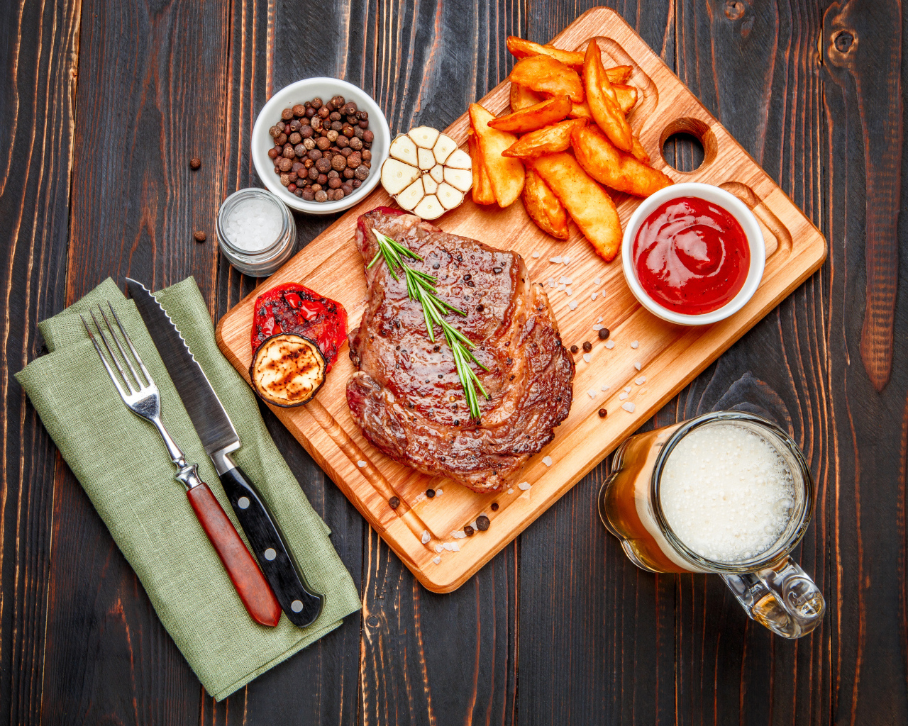 Сочный кусок мяса с картофелем фри, специями и бокалом пива на толе