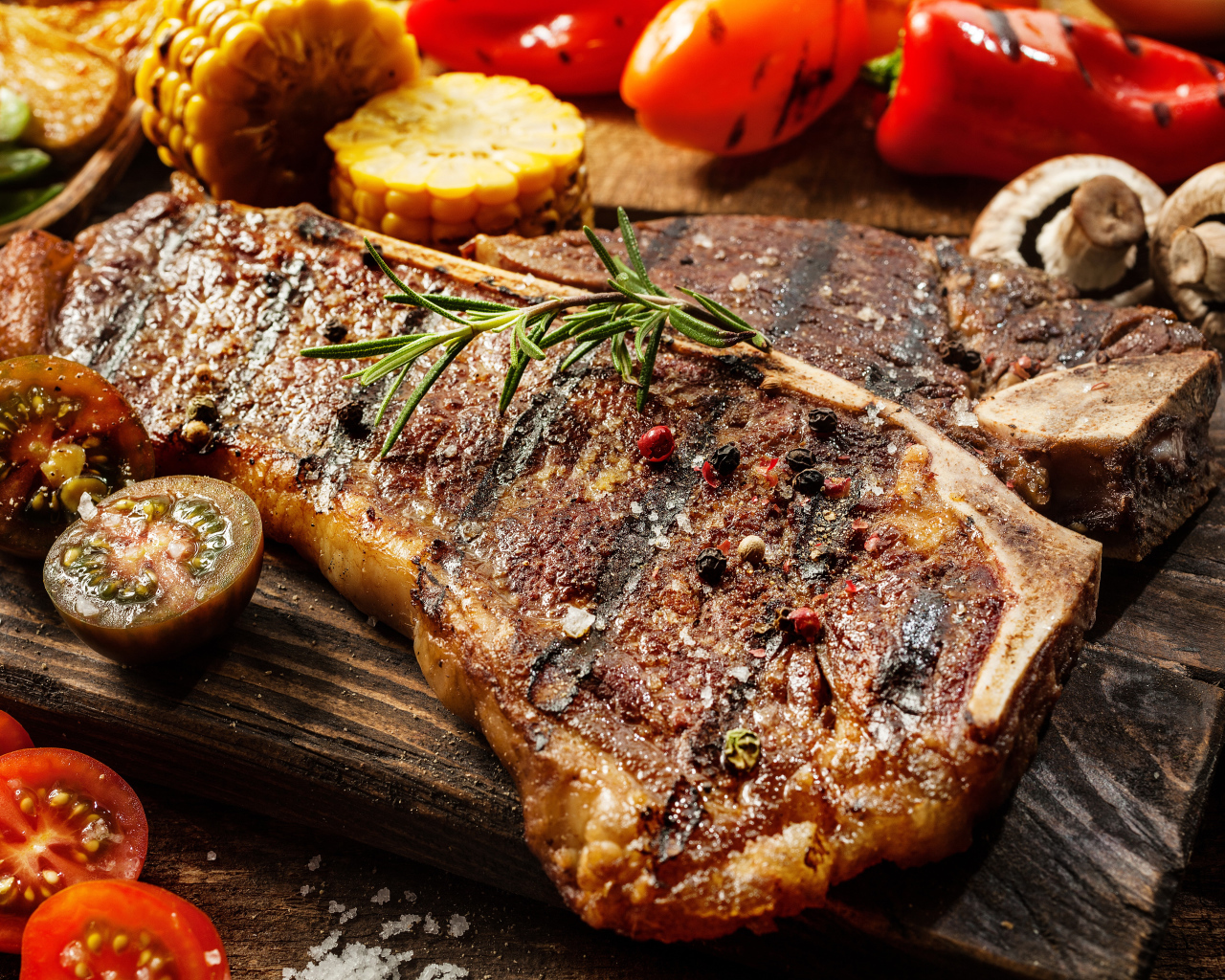 Кусок сочного жареного мяса на разделочной доске с овощами