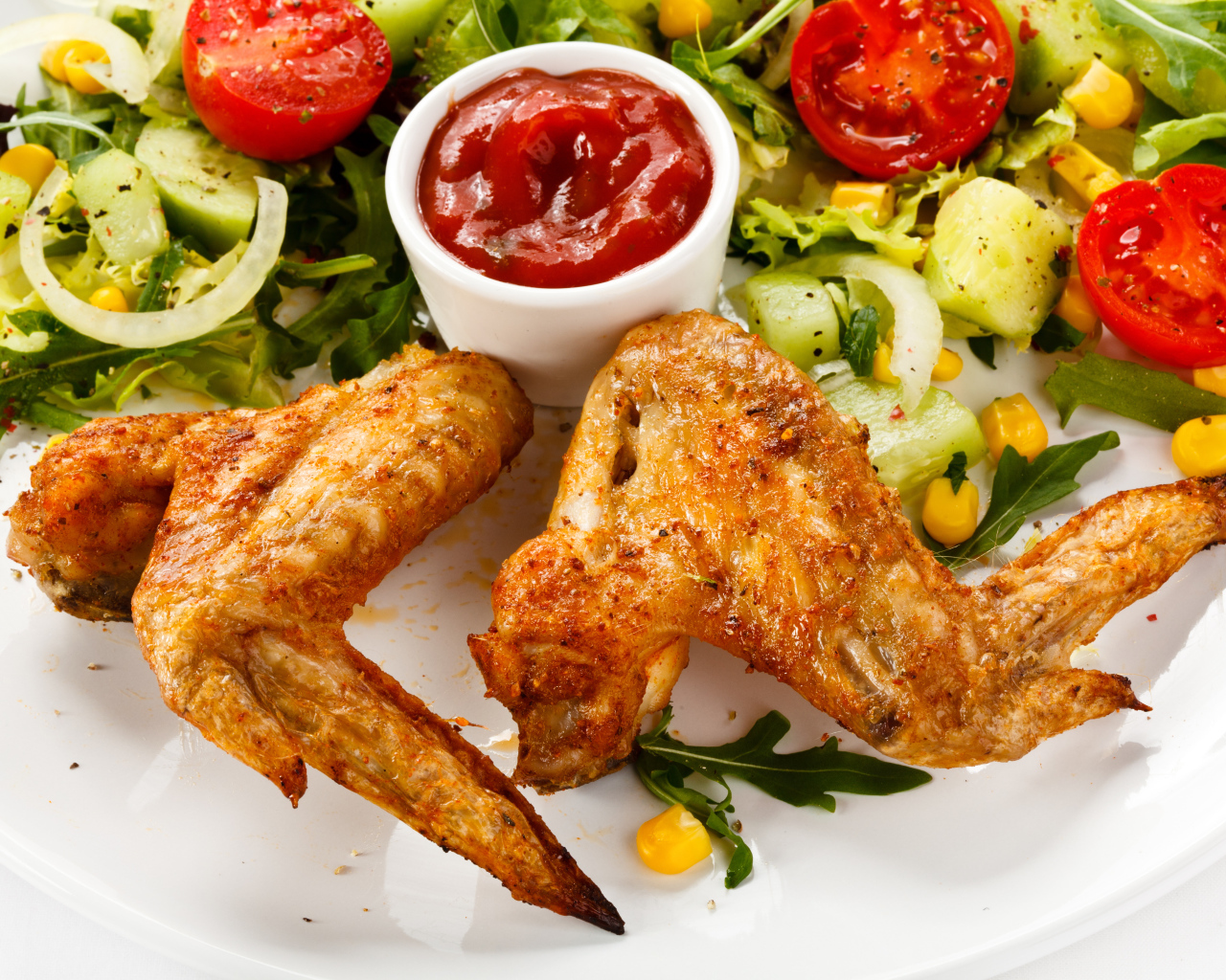 Жареные куриные крылышки с овощами и кетчупом на белой тарелке
