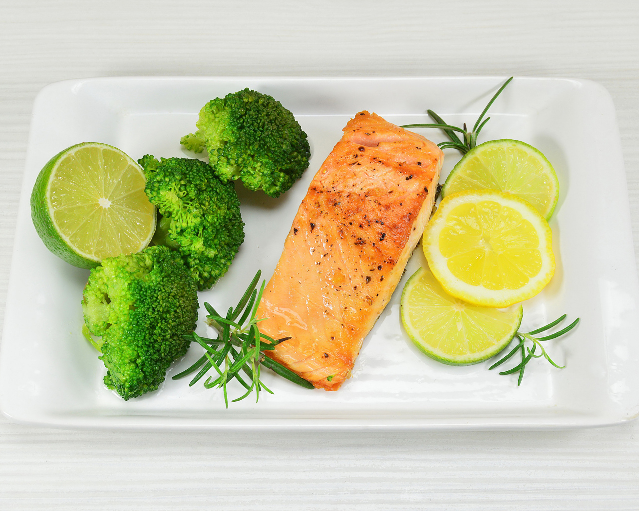 Красная рыба на белой тарелке с лимонами и брокколи